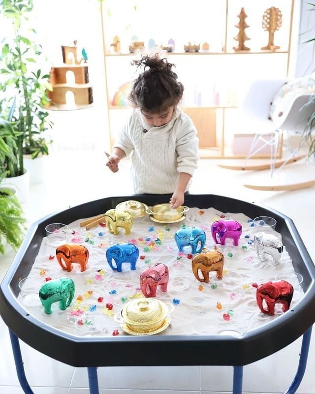Kleuter speelt met kleurrijke olifanten en juwelen in een tuff tray
